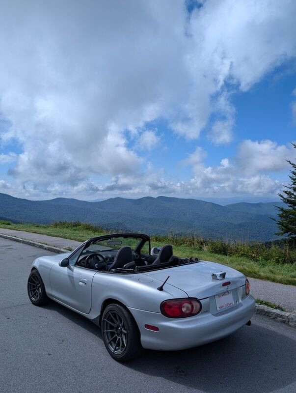 The Miata parked at a Blue Ridge Parkway overlook, top down, mountains behind.