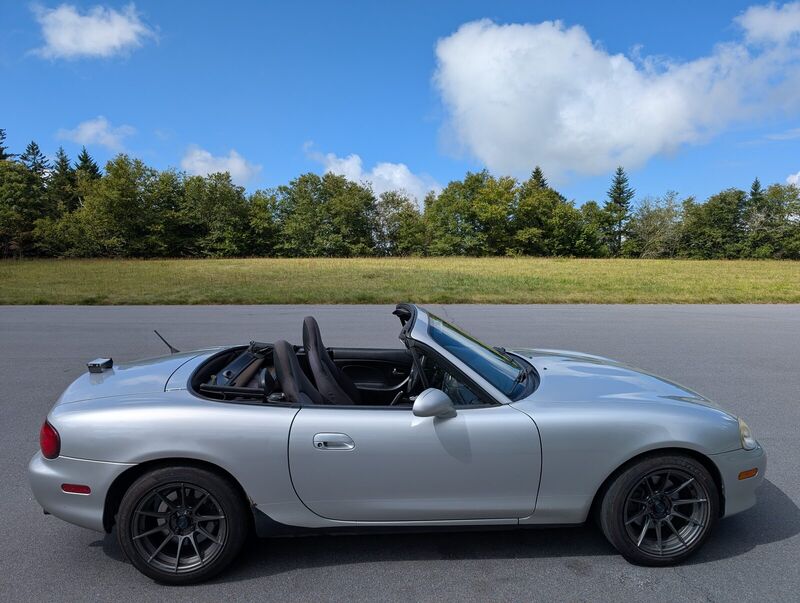 Side profile of the Miata parked on a country road with the top down under a bright cloudy sky.