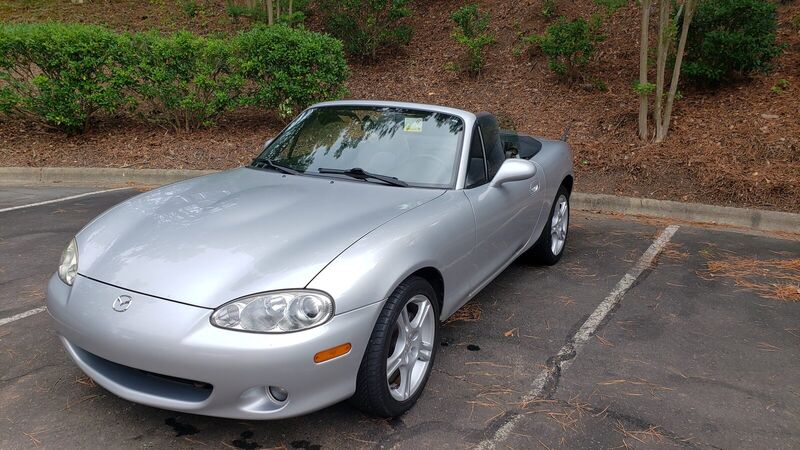 The Miata parked beside a landscaped bank a few weeks after purchase, still on its original wheels.