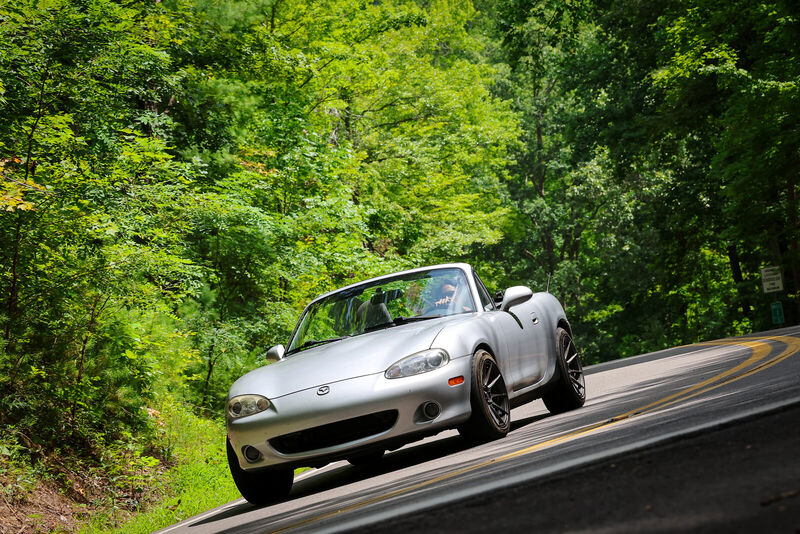 The Miata climbing a corner on the Tail of the Dragon, trees close on both sides.