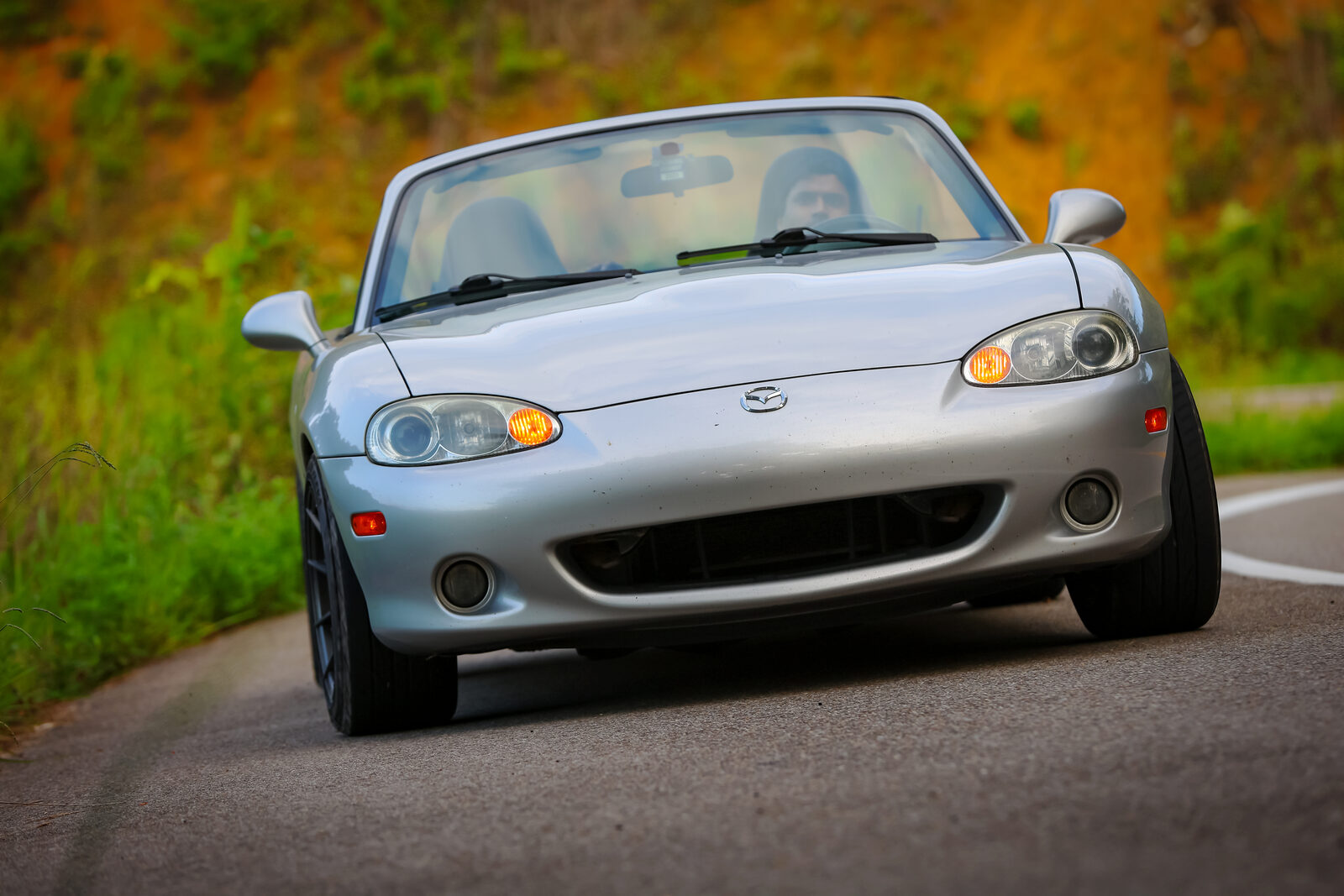 The Miata mid-corner on the Tail of the Dragon with the top down, leaning on its outside front wheel, driver visible.